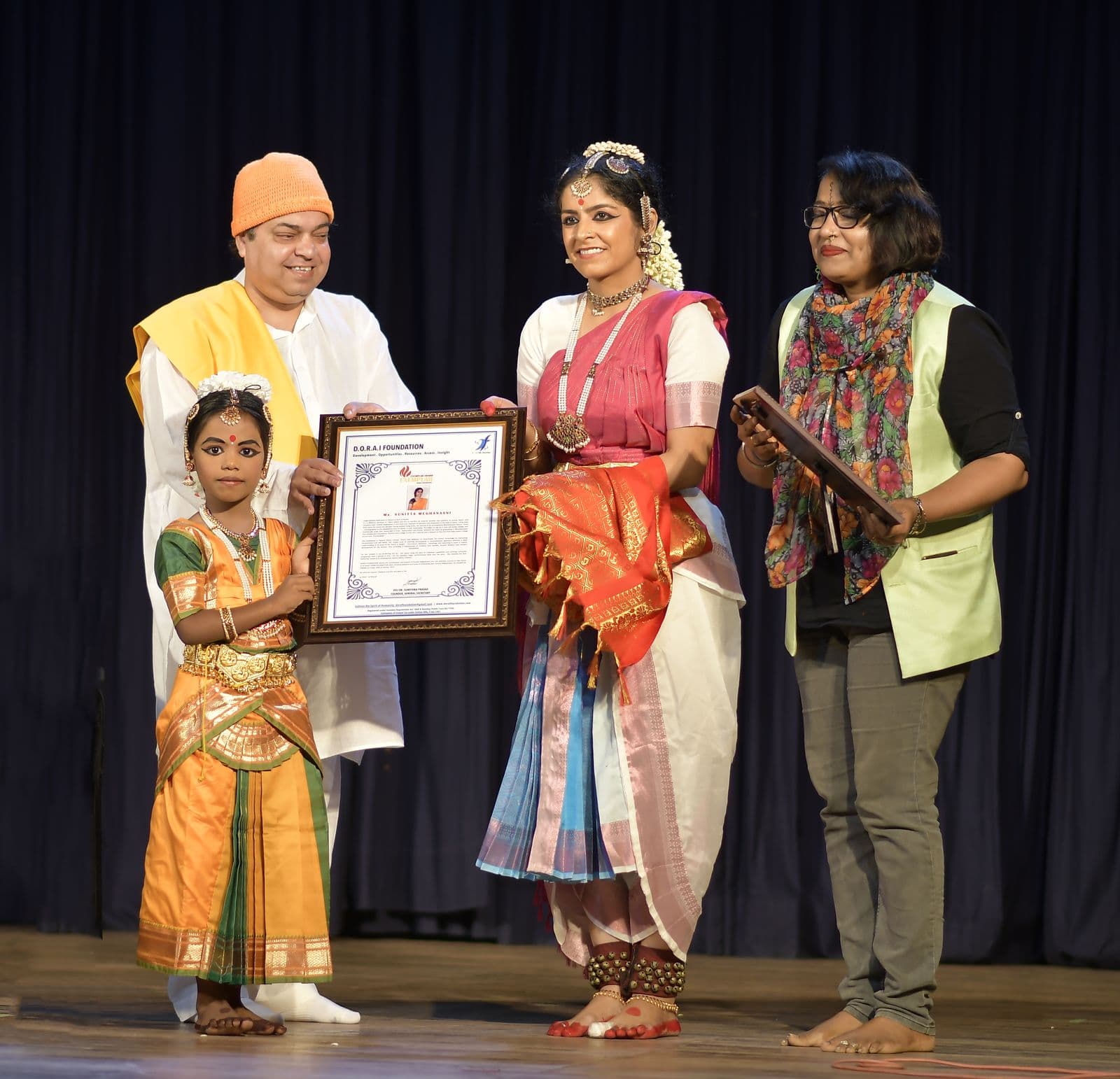 Sunitta Menghanaani receiving an award on stage, with Om Guru Om beside her