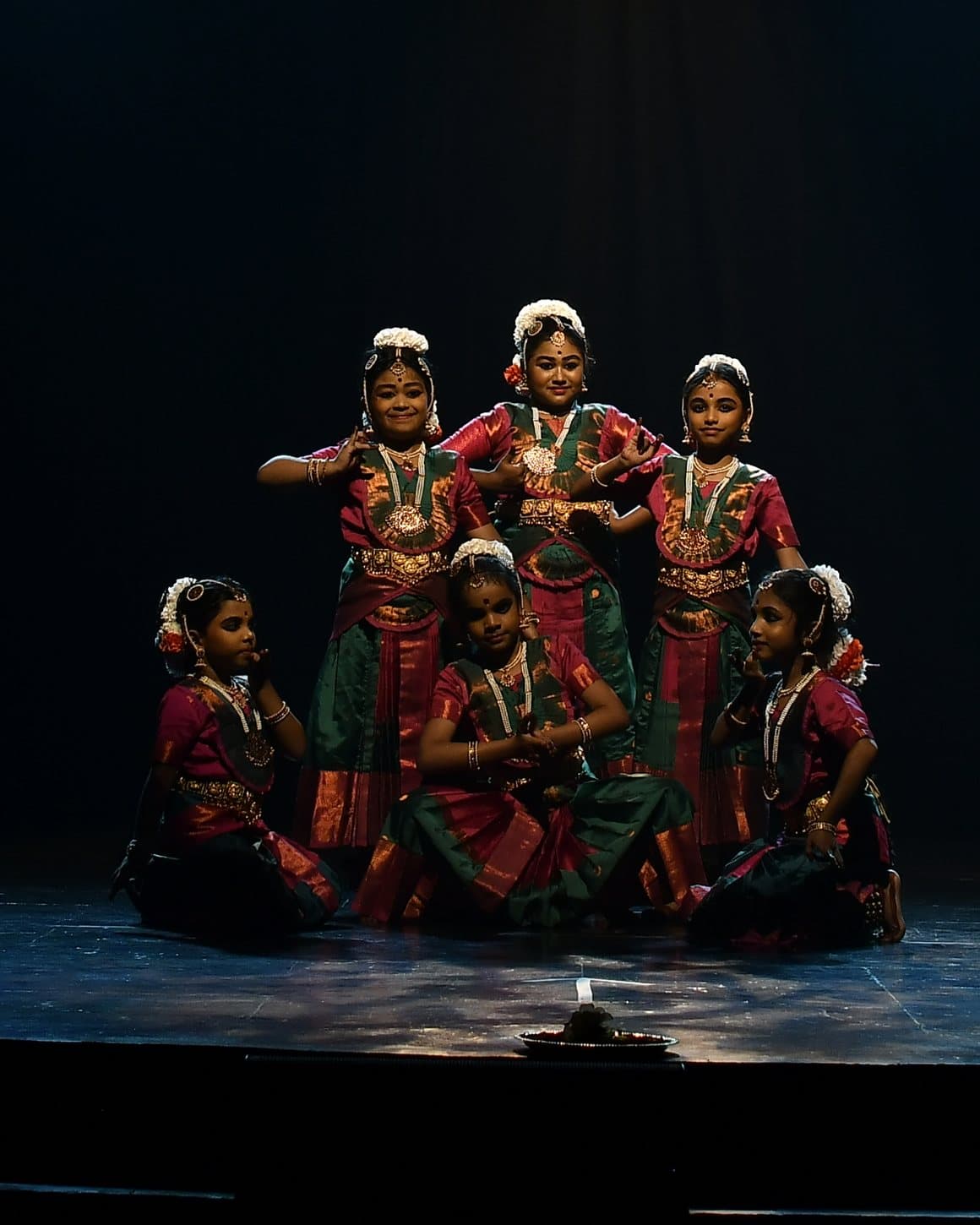 Six dancers at Udaan 2025, three standing and three seated together under a single spotlight