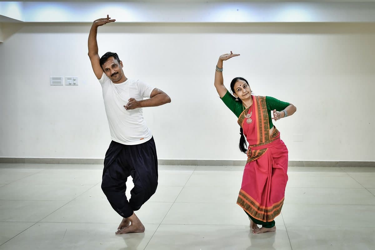 Two adults practising in class, both with one arm raised overhead and one hand at the waist