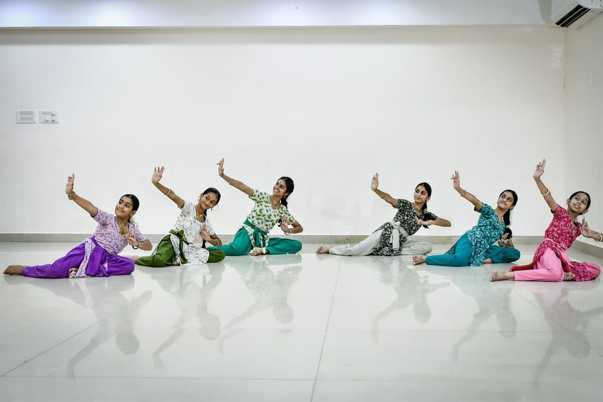 Six students seated in a row on the studio floor, each with one arm raised overhead and one held in front, at Appaswamy Springs